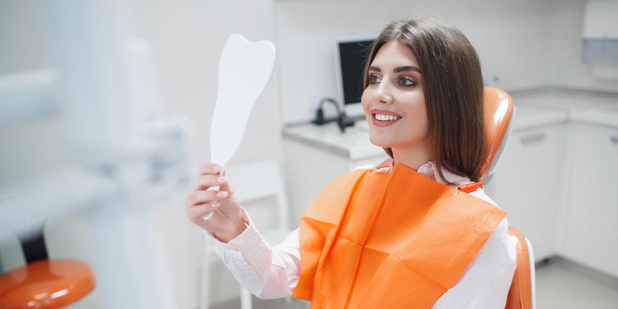 Nice lady with dark hair smiling looking into mirror because she went to Bonvallet Dental for Denture